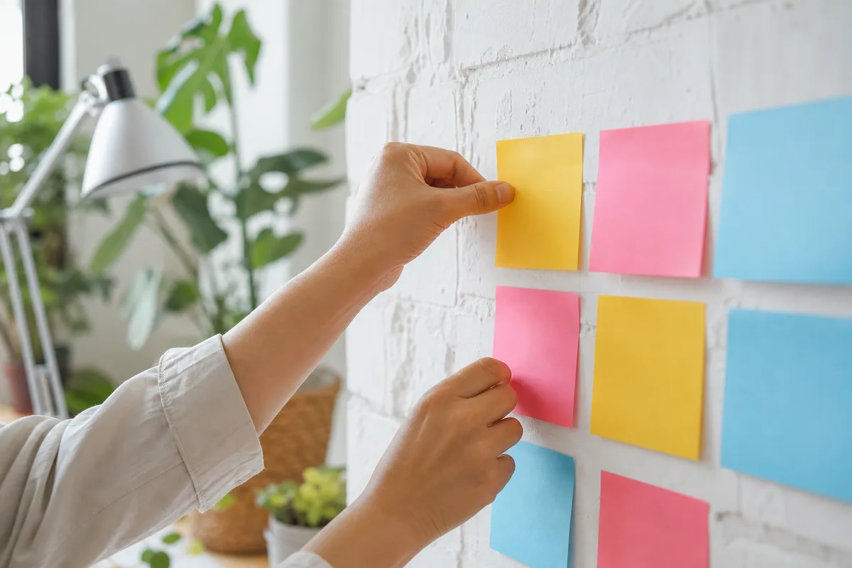 Mains collant des notes adhésives vierges colorées sur un mur blanc lumineux