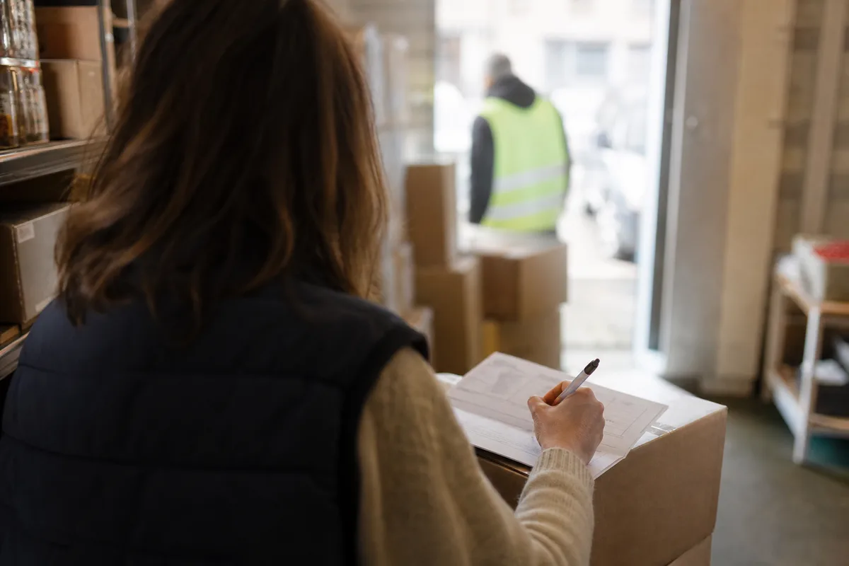 Commerçante notant des réserves sur un bon de livraison devant le livreur